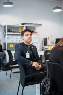 Darbnīcas dalībnieks sēž pie galda un klausās diskusiju.