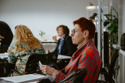 Darbnīcas dalībniece klausās diskusiju, turot rokā darba lapu un pildspalvu.