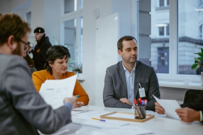 Darbnīcas dalībnieki pie galda apspriež izdrukātus darba materiālus.
